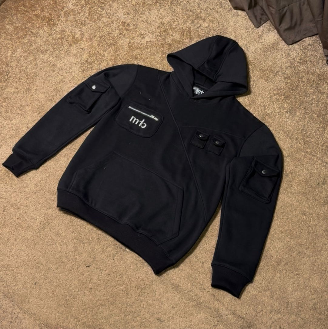 Black hoodie with a logo on the chest, laid flat on a carpeted floor.