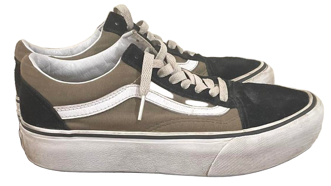 Pair of black and gray sneakers on a black cylindrical object against a beige wall.