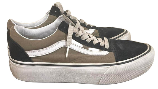 Pair of black and gray sneakers on a black cylindrical object against a beige wall.